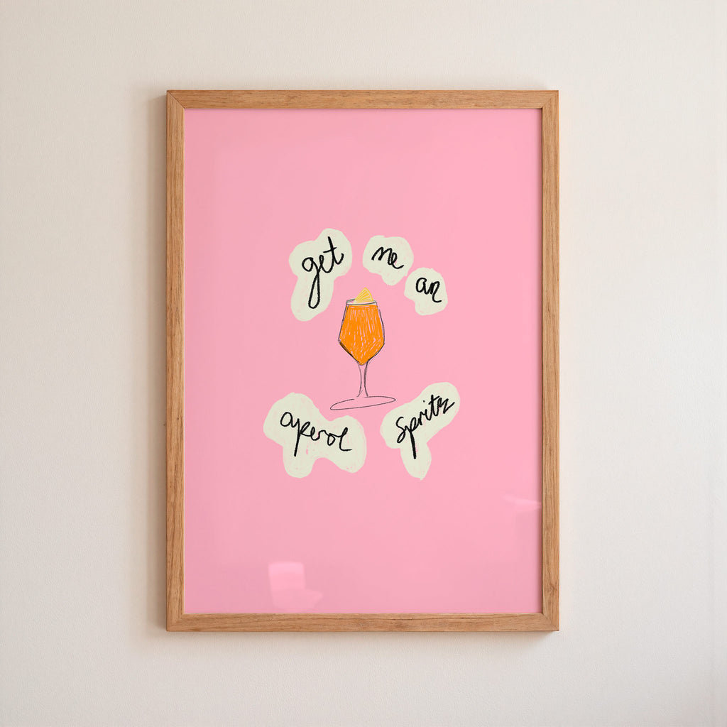 Framed pink poster with aperol spritz illustration and text on a beige wall.