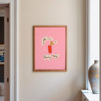 Modern kitchen with a pink framed picture on the wall, a vase of flowers on the counter, and a view into a living room.