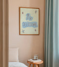 Framed artwork on a wall above a bed with a small table and books.