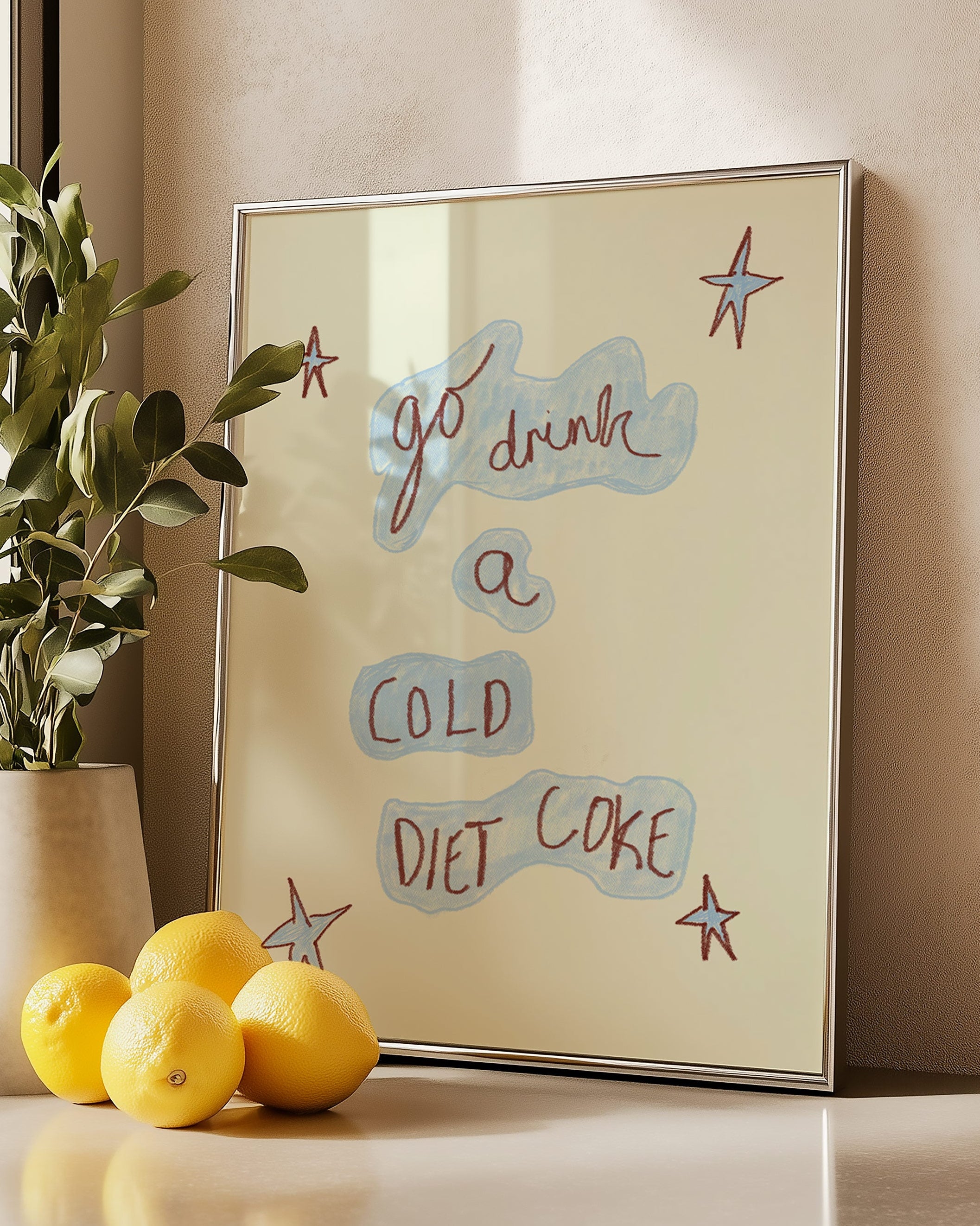 Silver frame with motivational quote 'go drink a cold diet coke', lemons, and plant on a surface.