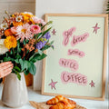 Person arranging flowers in a vase with a framed print that says 'go brew some nice coffee' and pastries on a table.