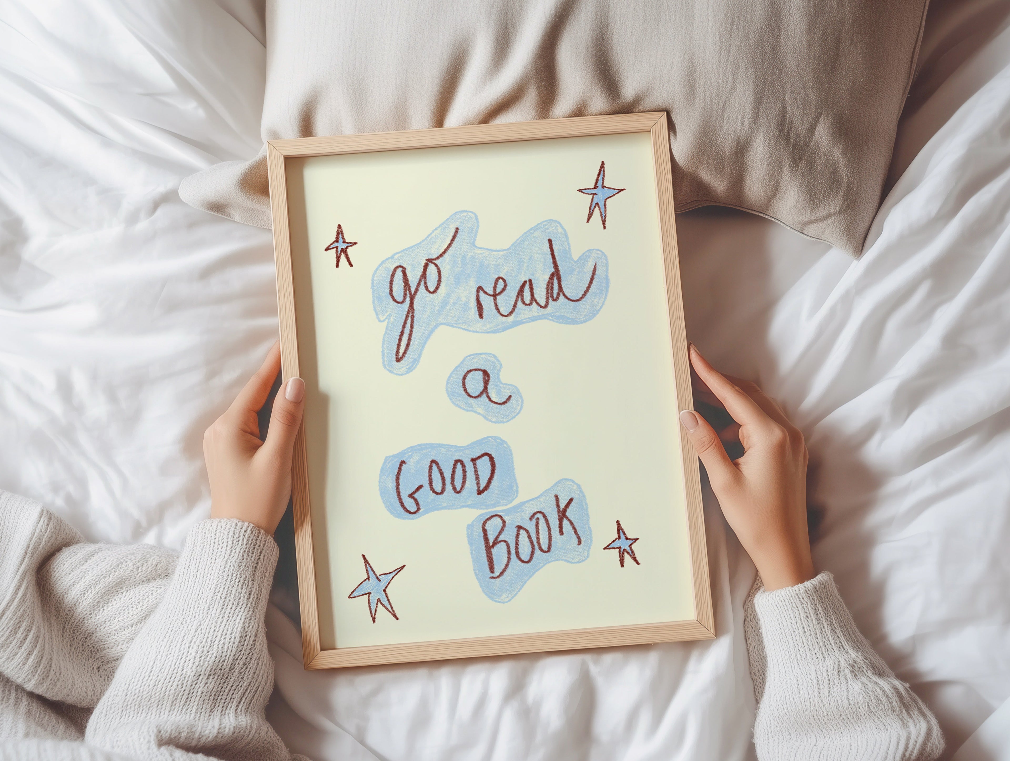 Person holding a framed quote 'go read a good book' on a bed.
