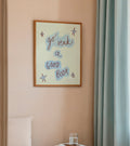 Framed artwork on a wall above a bed with a small table and books.