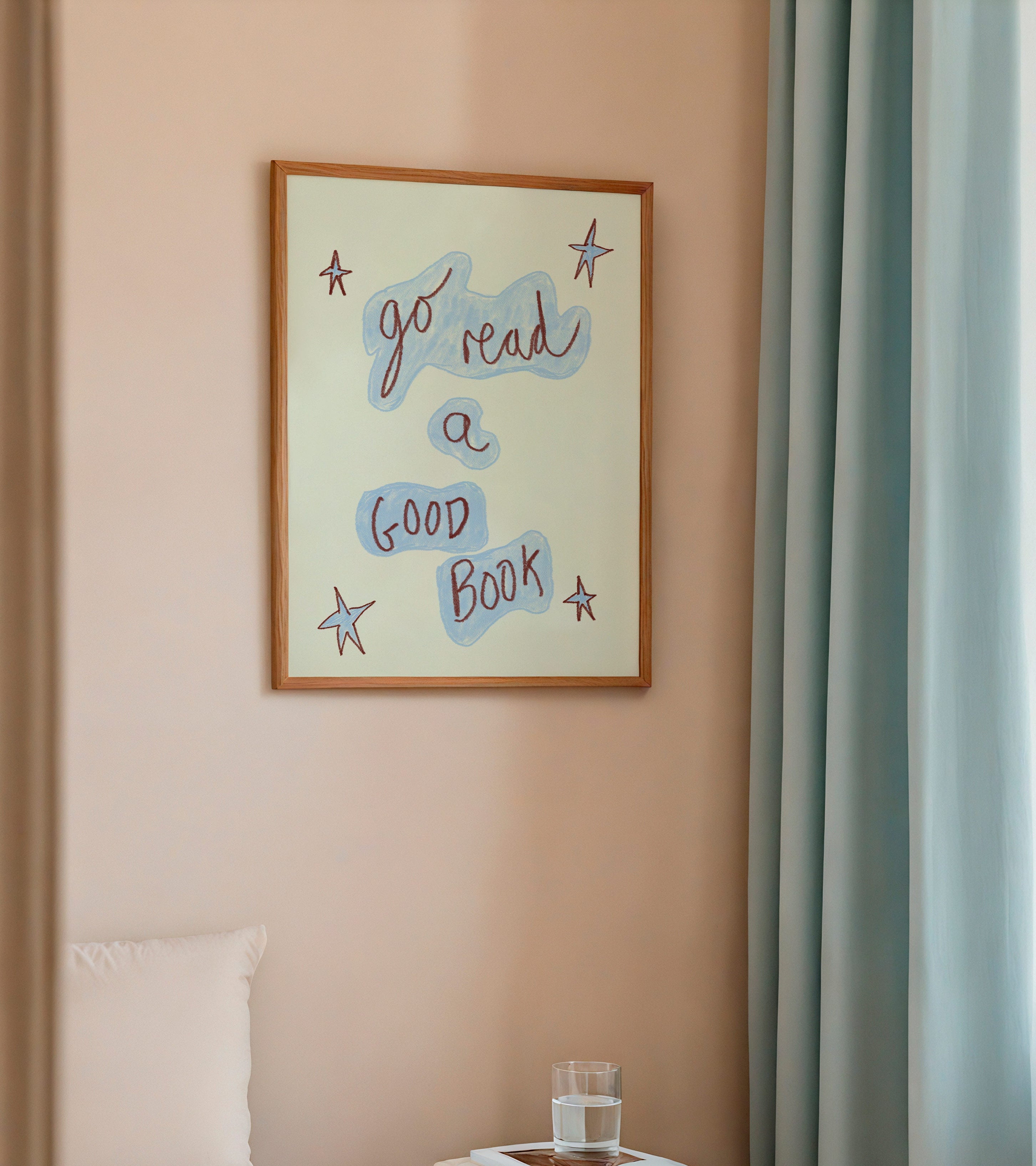 Framed artwork on a wall above a bed with a small table and books.