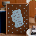 Decorative framed print with text on a table in a home setting