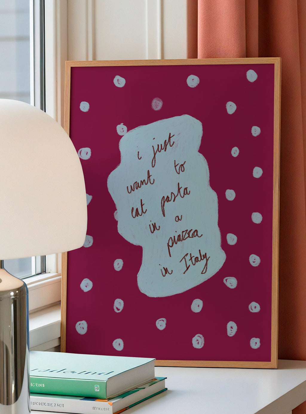Framed artwork with polka dots and text on a table with books and a lamp.