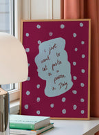 Framed artwork with polka dots and text on a table with books and a lamp.