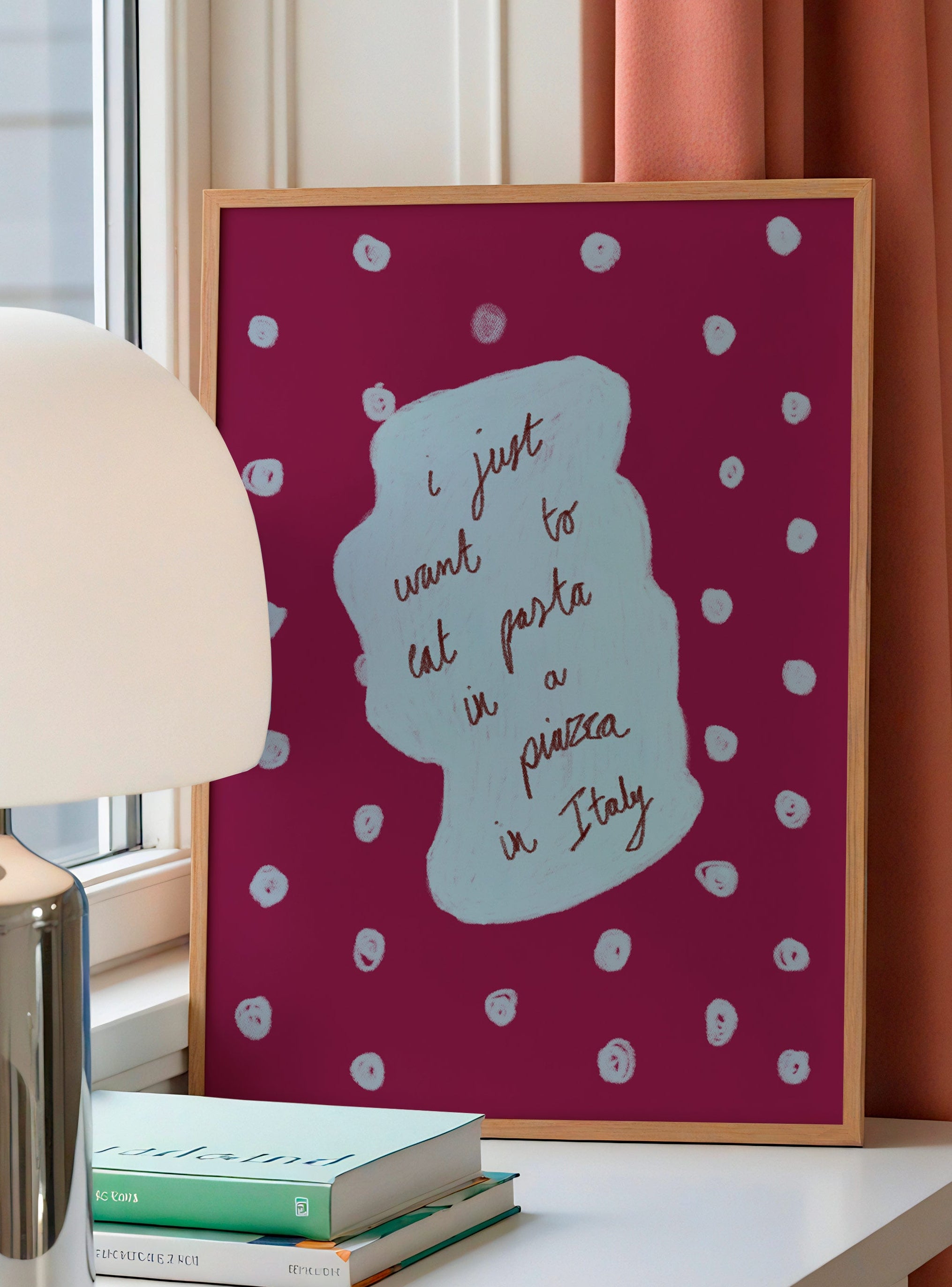 Framed artwork with polka dots and text on a table with books and a lamp.