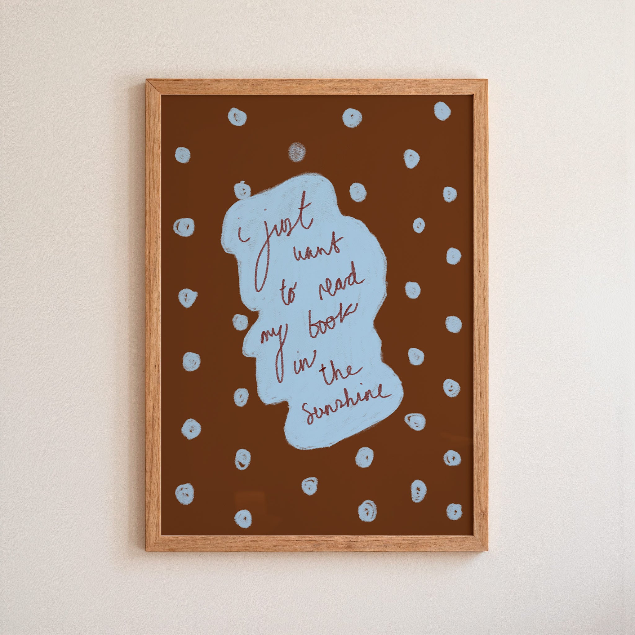 Framed artwork with text 'I just want to read my book in the sunshine' on a brown background with white polka dots.