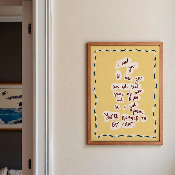 Yellow 'eat cake' print in a Modern kitchen with a blue island, white cabinets, and a view into a living room.