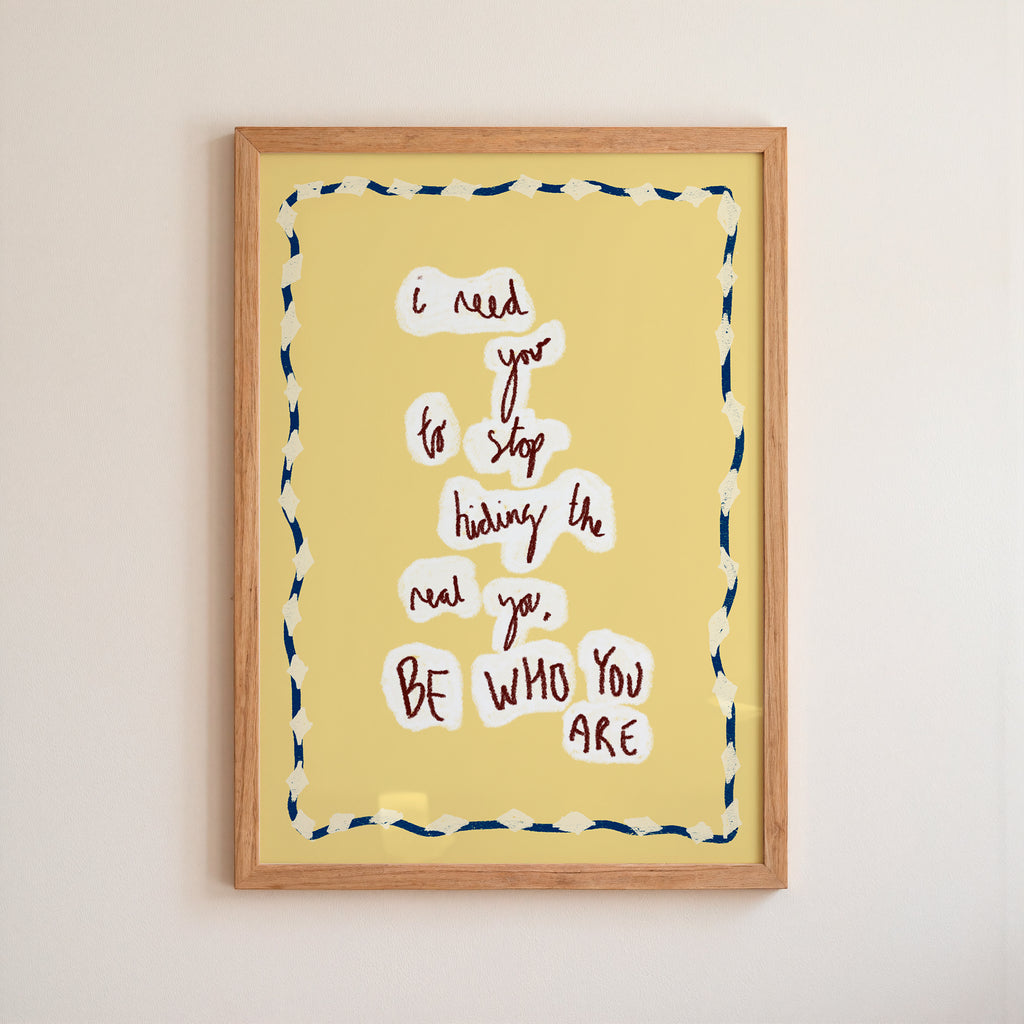 Yellow motivational 'be who you are' poster in a frame on white wall