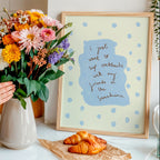 Person arranging flowers on a kitchen counter with a framed picture and pastries in the background.