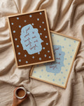 Two framed prints with polka dots and text on a beige fabric background, with a hand holding a mug.