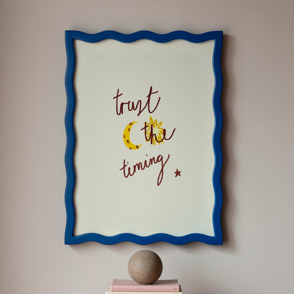 Framed artwork with motivational quote which reads 'trust the timing' on a wall above books