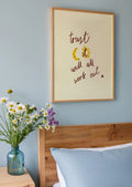 Bedroom with wooden headboard, blue pillows, and a vase of flowers on a nightstand. Framed print with 'trust it ill all work out