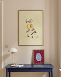 Framed artwork with phrase 'trust it will all be worth it' on a wall above a blue table with a lamp and book.