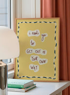 Yellow framed poster with motivational quote on a desk with books and a lamp.